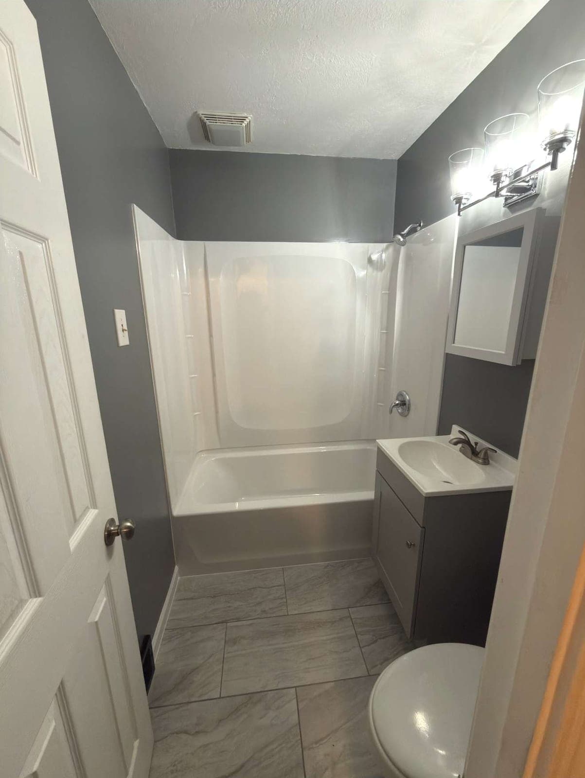 Remodeled bathroom with new tub surround, gray vanity and large-format tile floor