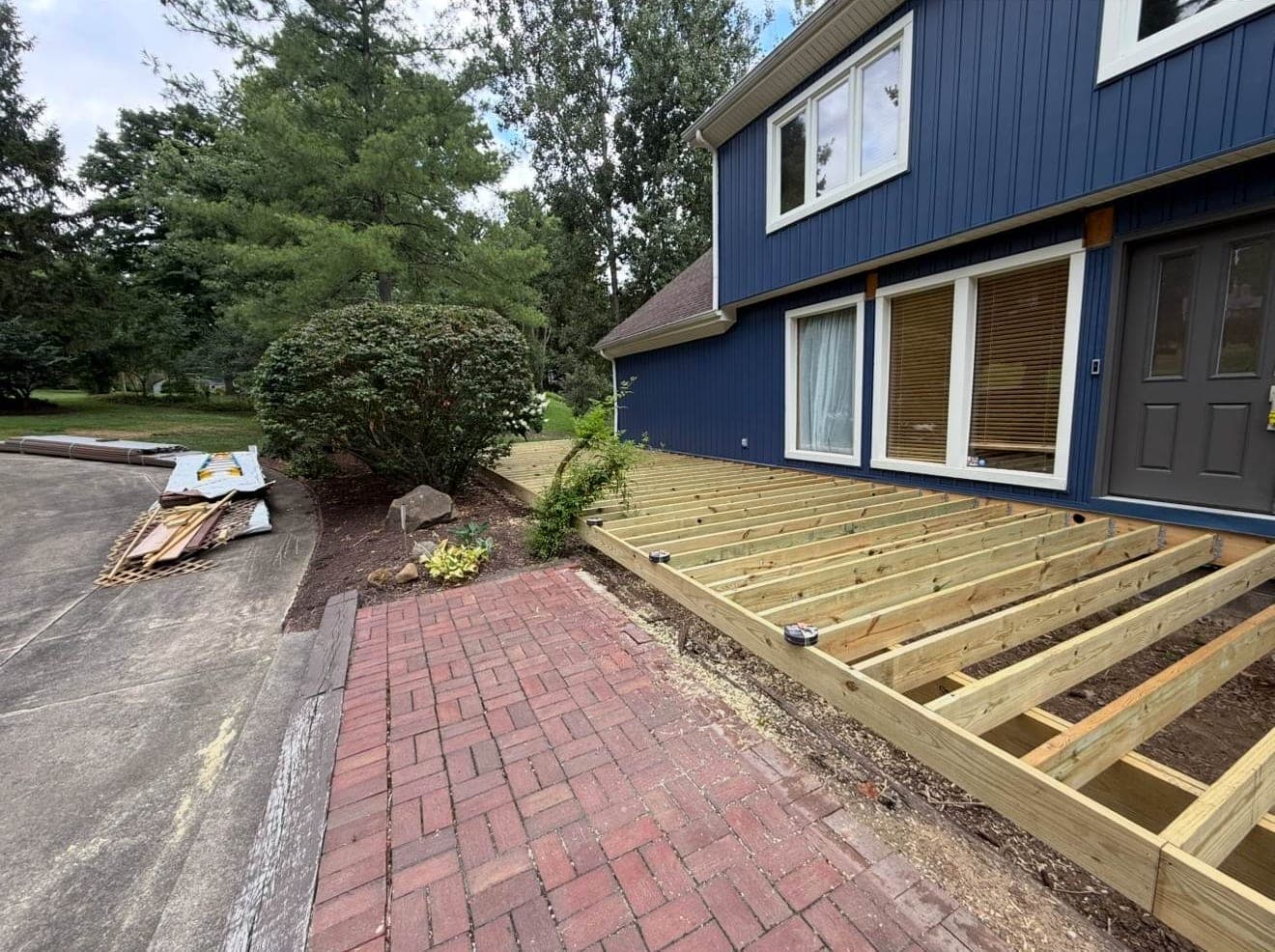 New deck framing going up beside a backyard patio