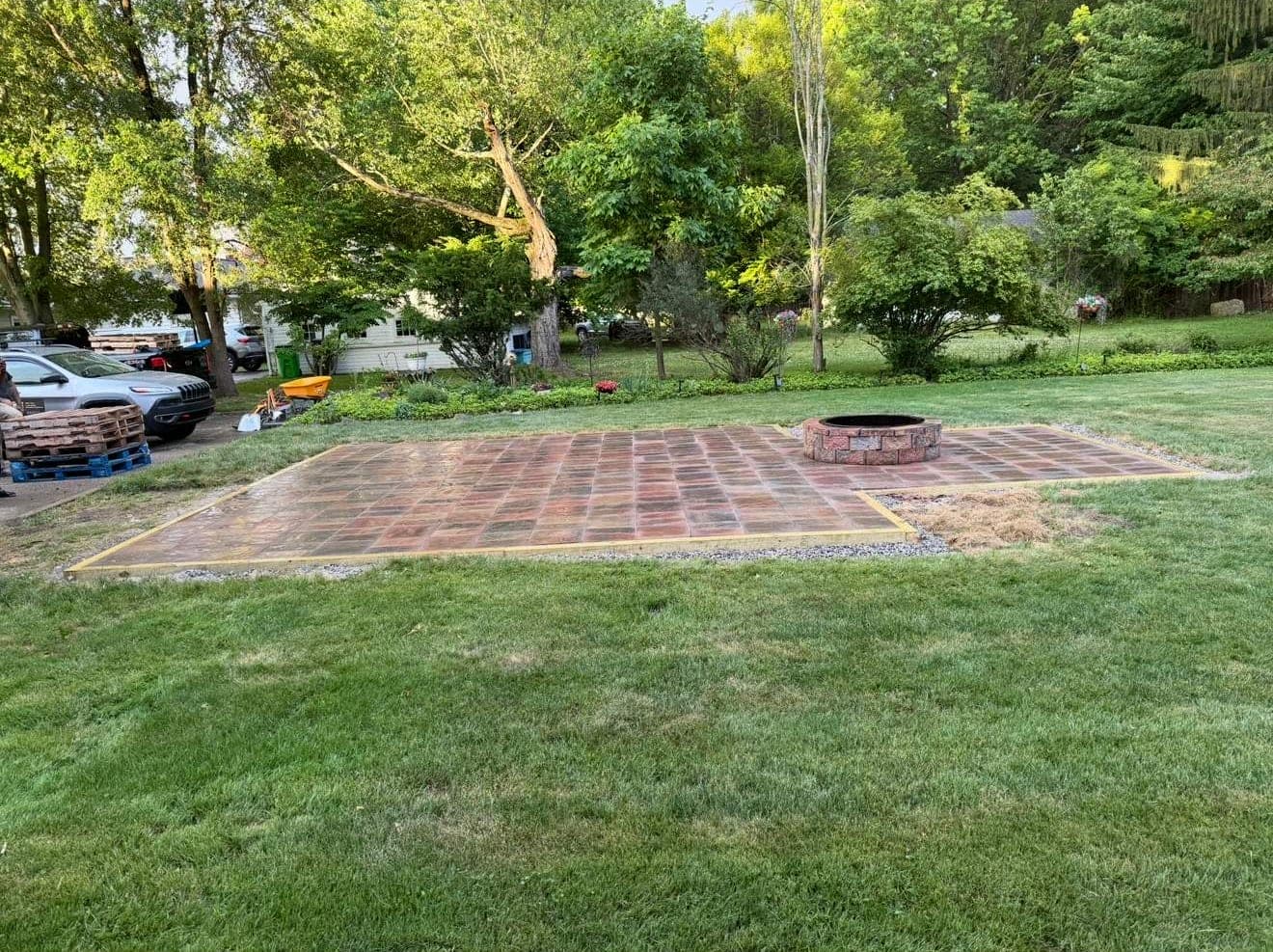 New brick paver patio with a built-in fire pit in a green backyard