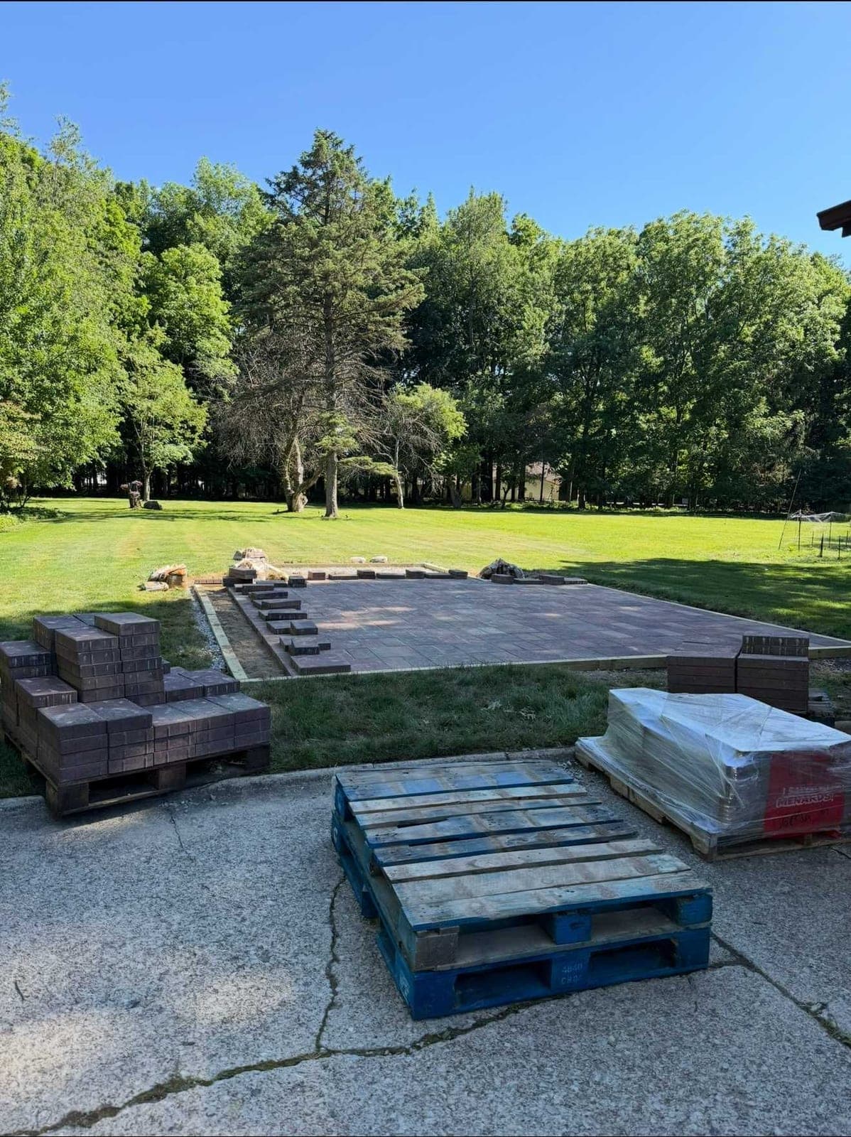Pallets of pavers beside a patio being laid in a backyard